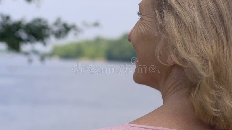 Glückliche lächelnde alte Frau, die in der Natur sich entspannt und oben See, Abschluss betrachtet