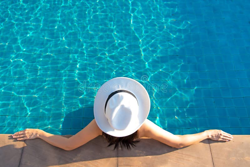 Glückliche lächelnde asiatische Frau mit Strohhut entspannen sich und Luxus im Swimmingpool am Urlaubshotel, am Lebensstil und am