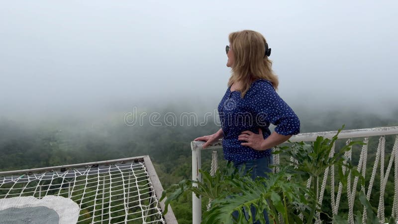 Glückliche lächelnde Frau am grünen Abgrund mit dicken Nebel auf einem Aussichtspunkt mit Hängematte hoch in den Bergen am Rand