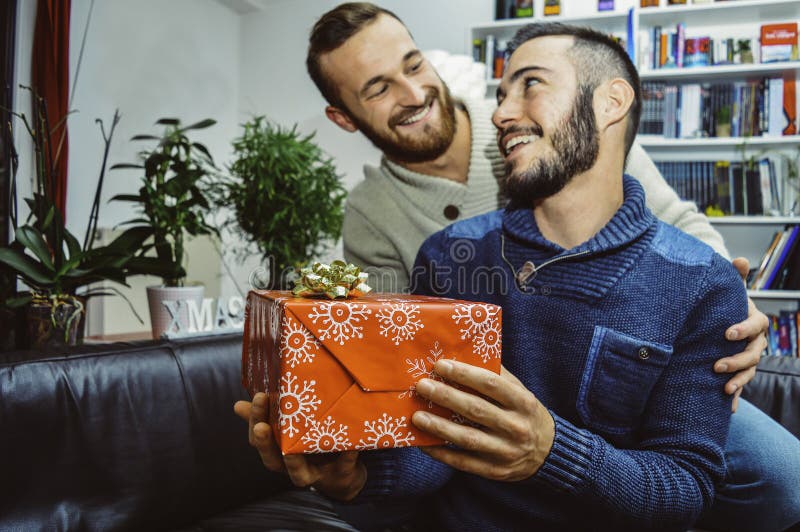 Glückliche lächelnde junge hübsche homosexuelle Paare in der Liebe, die einander Geschenk feiernd und gebend betrachtet lizenzfreies stockfoto Glückliche lächelnde junge hübsche homosexuelle Paare in der Liebe, die einander Geschenk feiernd und gebend betrachtet lizenzfreies stockfoto