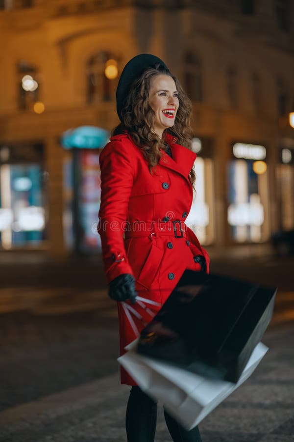 Winter Fun. happy trendy tourist woman in red coat and black beret with shopping bags outside in the city at night. Winter Fun. happy trendy tourist woman in red coat and black beret with shopping bags outside in the city at night