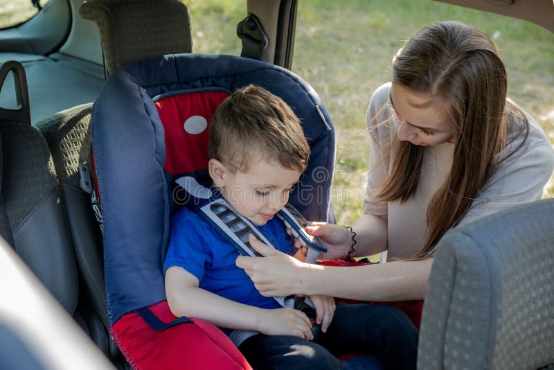 Glückliche Mutter, die ihren Sohn in einem Kindersitz betrachtet. Jung weibliches vorbereitendes Kind für eine Reise. Sicherheit lizenzfreie stockfotografie