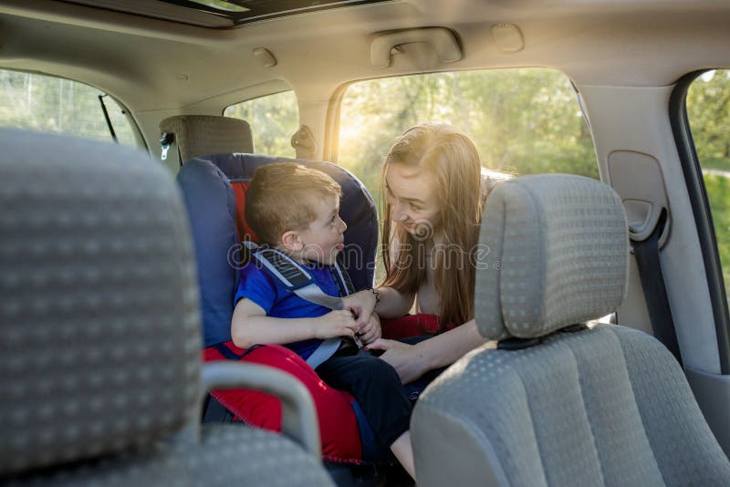 Glückliche Mutter, die ihren Sohn in einem Kindersitz betrachtet. Jung weibliches vorbereitendes Kind für eine Reise. Sicherheit lizenzfreies stockfoto