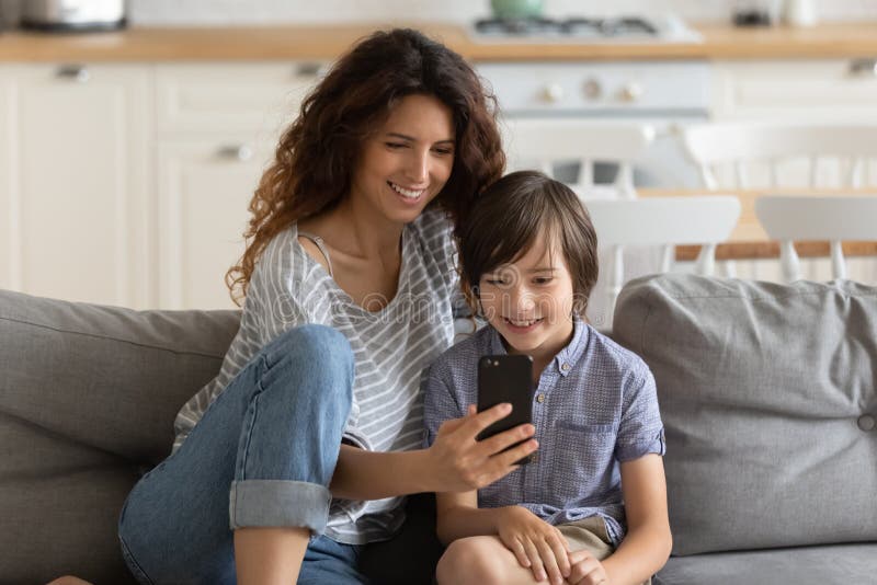 Glückliche Mutter haben Spaß mithilfe des Smartphone mit wenig Sohn. Glückliche junge Mutter, auf die Couch zu sitzen haben Spaß lustige Videos auf Zelle mit wenig Vorschülersohn, Lächeln Mutter schaut und kleine Jungenkind lockern sich das Sofa zu Hause mithilfe des Navigieren Smartphonegeräts zusammen