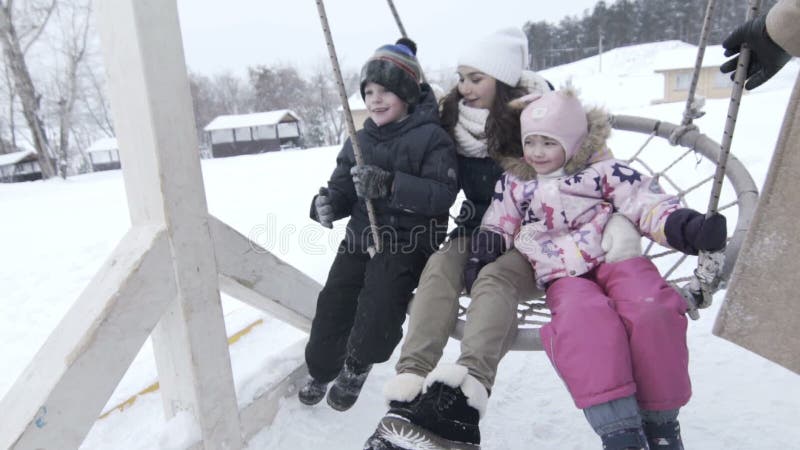 Glückliche Mutter mit zwei Kindern auf großem Schwingen im Winter, slowmotion