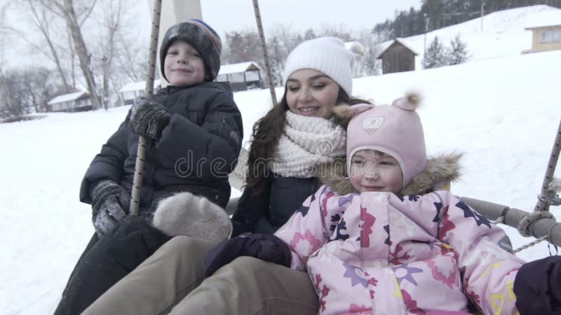 Glückliche Mutter mit zwei Kindern auf großem Schwingen im Winter, slowmotion