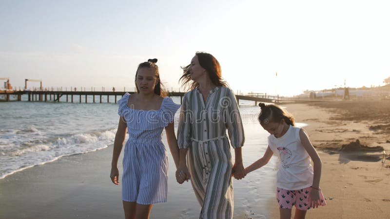 Glückliche Mutter mit zwei Töchtern 7 und 13 Jahre Spaziergang auf dem Sandstrand bei Sonnenuntergang