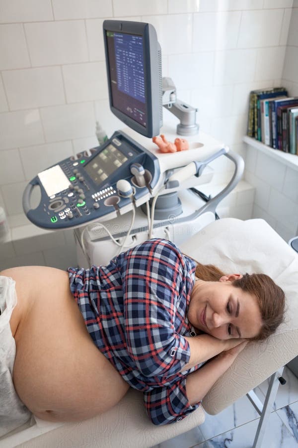 Glückliche schwangere Frau, bevor Ultraschallscan vom Geburtshelfer in der Klinik, Lügenseitenlage erhalten wird