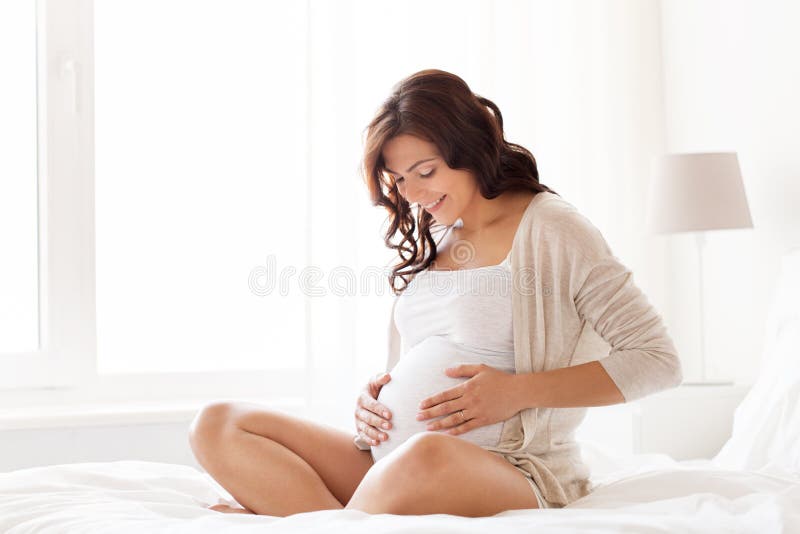 Glückliche schwangere Frau, die zu Hause auf Bett sitzt