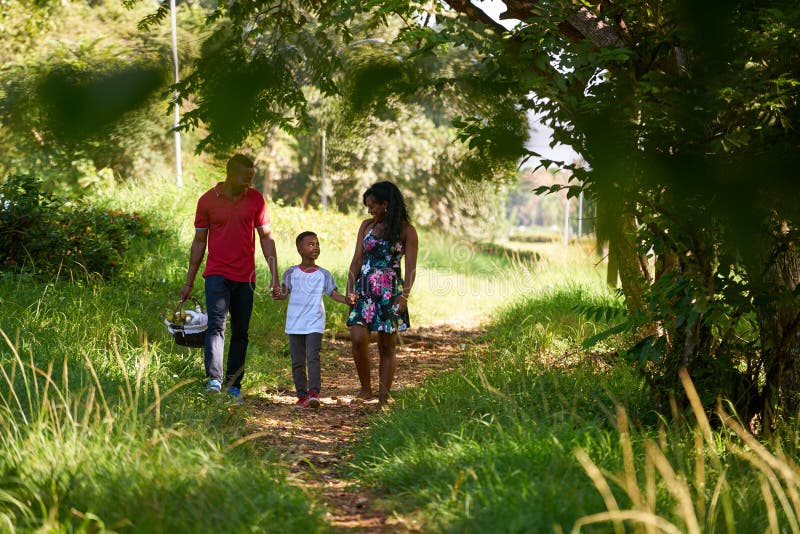 Glückliche schwarze Familie, die in Stadt-Park mit Picknick-Korb geht