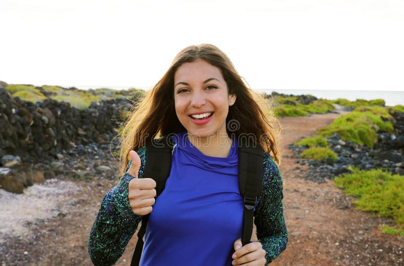 Glückliche wandernde Frau, welche die oben lächelnden Daumen gibt Junges Wandererfrauenlächeln froh an der Kamera im Freien auf W