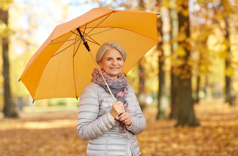 Glückliche ältere Frau mit Regenschirm am Herbstpark lizenzfreie stockbilder Glückliche ältere Frau mit Regenschirm am Herbstpark lizenzfreie stockbilder