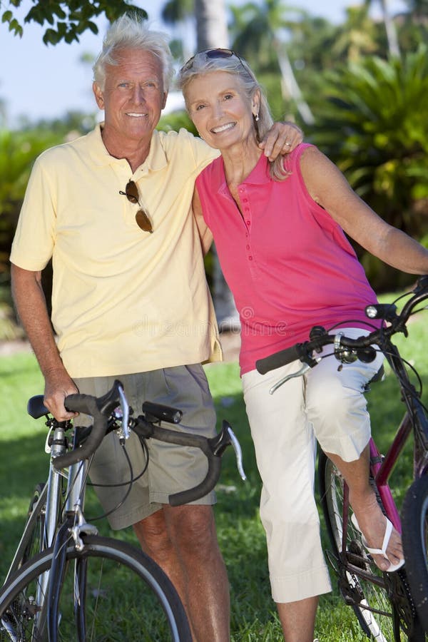 Happy senior man and woman couple together cycling on bicycles outside in a sunny green park. Happy senior man and woman couple together cycling on bicycles outside in a sunny green park