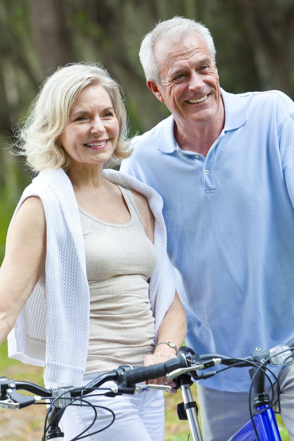 Happy senior men and women couple sitting together smiling and happy with bicycles at a park. Happy senior men and women couple sitting together smiling and happy with bicycles at a park