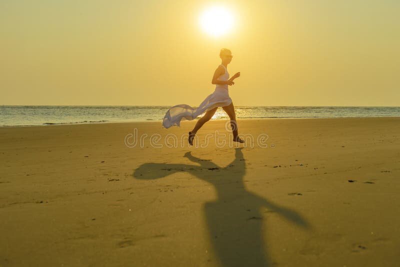 Glücklichen jungen kaukasischen Blondine in der Sonnenbrille und in flatternden weißen Kleiderläufen hinunter den Strand bei Sonn lizenzfreies stockbild Glücklichen jungen kaukasischen Blondine in der Sonnenbrille und in flatternden weißen Kleiderläufen hinunter den Strand bei Sonn lizenzfreies stockbild