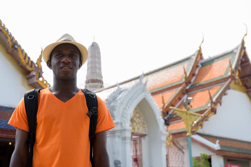 Glücklicher afrikanischer touristischer Mann, der am buddhistischen Tempel lächelt und denkt lizenzfreies stockfoto Glücklicher afrikanischer touristischer Mann, der am buddhistischen Tempel lächelt und denkt lizenzfreies stockfoto