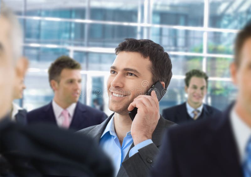 Happy businessman talking on mobile standing in crowd in office lobby. Happy businessman talking on mobile standing in crowd in office lobby.