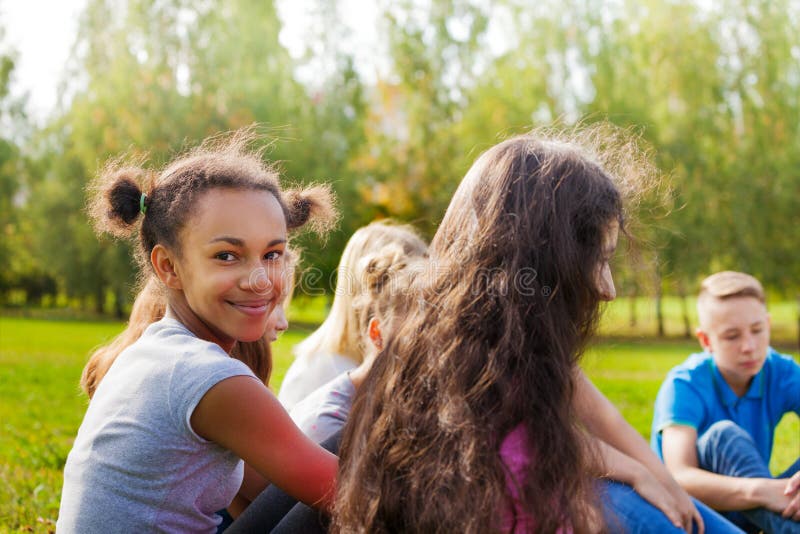 Glücklicher internationaler Teenager sitzt zusammen auf Wiese stockbild