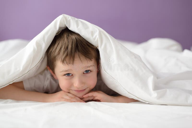 Glücklicher Junge, der im Bett unter einer weißen Decke oder einer Bettdecke sich versteckt stockfotos Glücklicher Junge, der im Bett unter einer weißen Decke oder einer Bettdecke sich versteckt stockfotos
