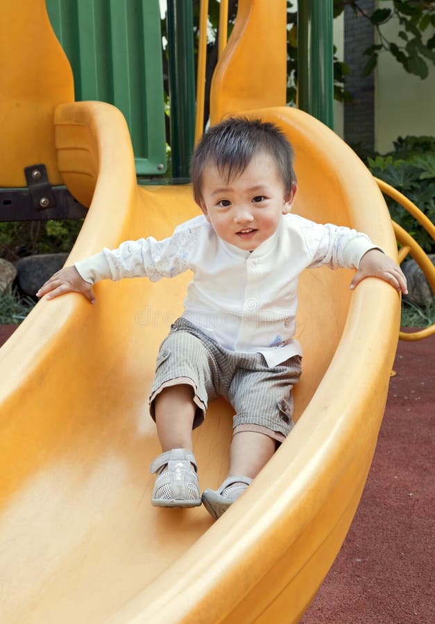 A happy Chinese boy smiles as he slides down a bright yellow slide at a playground. A happy Chinese boy smiles as he slides down a bright yellow slide at a playground.