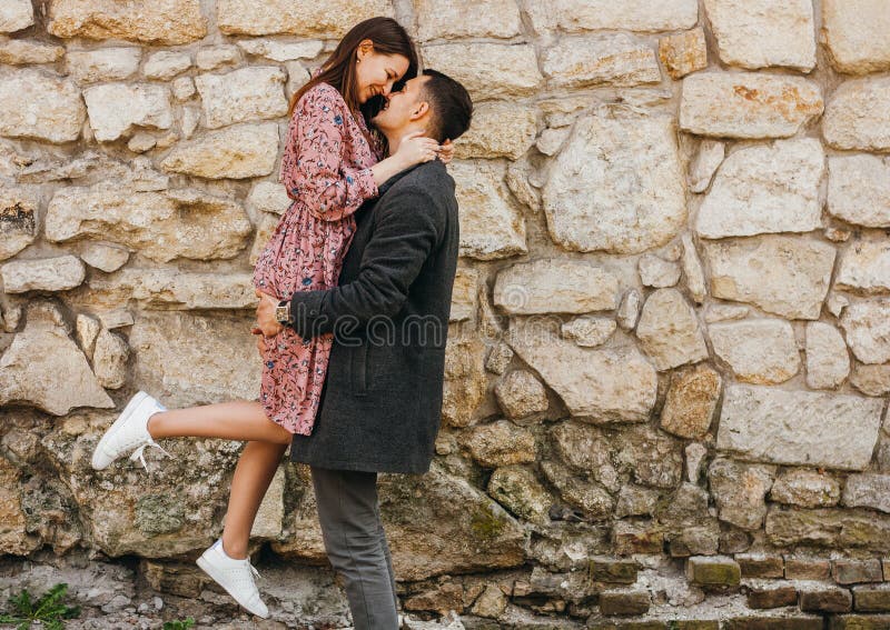 Gl?cklicher junger Mann, der seine Frau in seinen Armen gegen Steinhintergrund h?lt stockfotografie Gl?cklicher junger Mann, der seine Frau in seinen Armen gegen Steinhintergrund h?lt stockfotografie