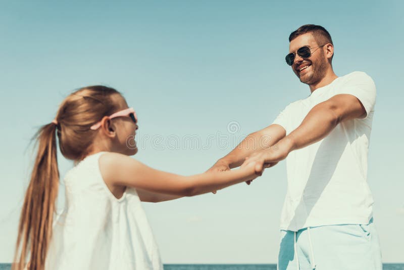 Glücklicher junger Vater in der Sonnenbrille dreht sich mit Tochter, Händchenhalten lizenzfreie stockbilder Glücklicher junger Vater in der Sonnenbrille dreht sich mit Tochter, Händchenhalten lizenzfreie stockbilder