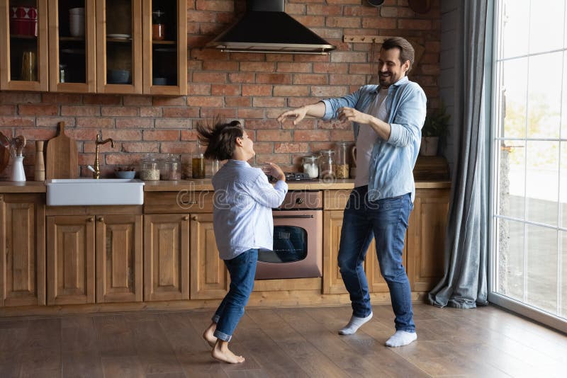Glücklicher junger Vater kleiner Sohn tanzt auf dem Boden in der Küche lizenzfreies stockfoto
