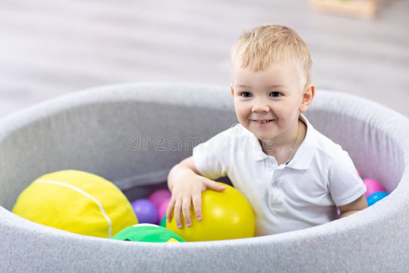 Glücklicher Kinderjunge, der den Spaß Innen in der Spielmitte hat Kind, das mit bunten B?llen im Spielplatzballpool spielt
