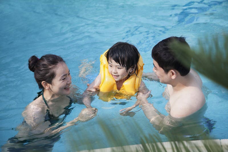 Glücklicher lächelnder unterrichtender Sohn der Familie, wie man im Pool schwimmt