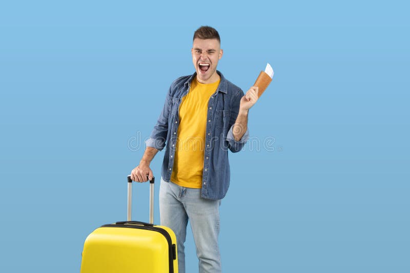 Glücklicher männlicher Tourist mit Koffer mit Pass und Tickets schreien mit Aufregung auf blauem Hintergrund Kopierraum lizenzfreie stockfotos