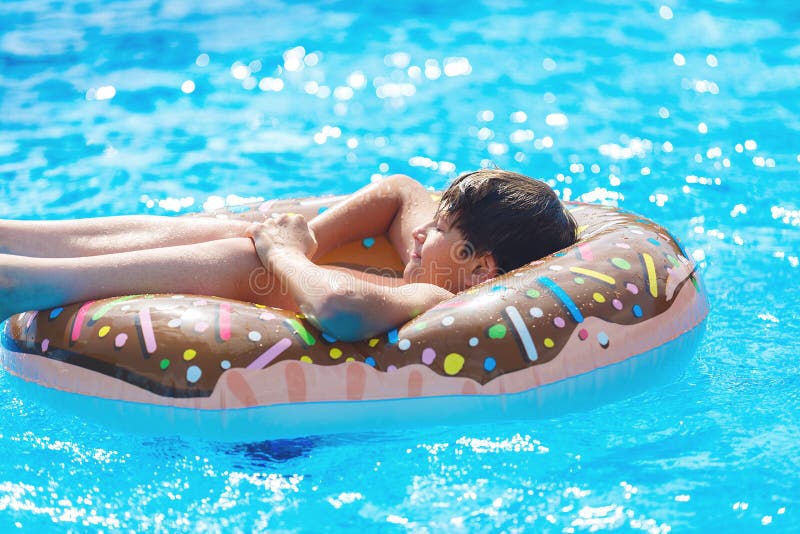 Glücklicher netter Jugendlicher des kleinen Jungen, der auf einem aufblasbaren Donutring im Swimmingpool liegt Aktive Spiele auf lizenzfreies stockbild Glücklicher netter Jugendlicher des kleinen Jungen, der auf einem aufblasbaren Donutring im Swimmingpool liegt Aktive Spiele auf lizenzfreies stockbild