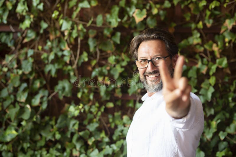 Glücklicher reifer Mann mit Brille und Siegeszeichen, während er gegen einen Kriecher steht, der das v-Zeichen zeigt. Portrait stockbilder
