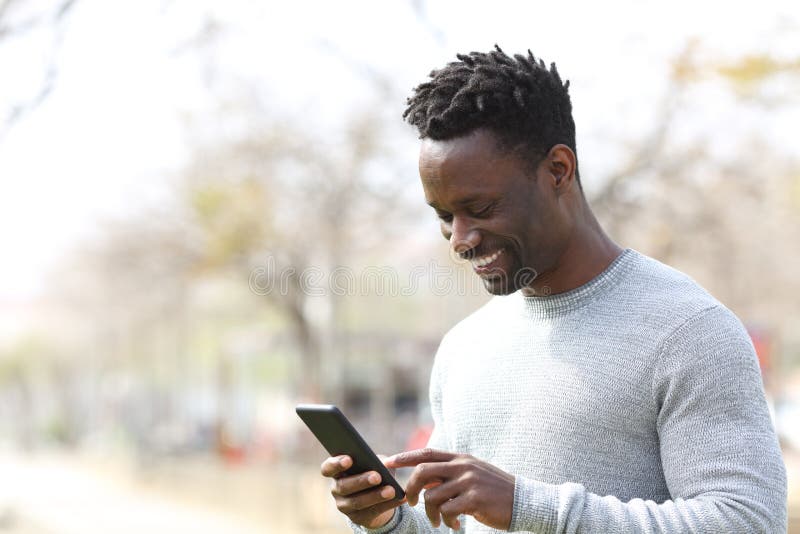 Glücklicher schwarzer Mann mithilfe des Smart Telefon in einem Park