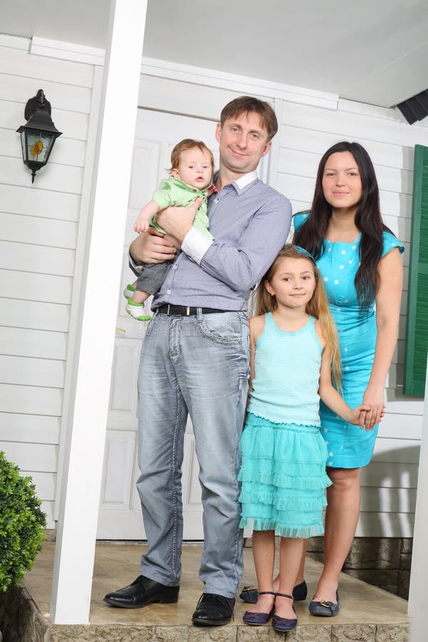 Glücklicher Stand der vierköpfigen Familie auf Portal des neuen Häuschens. lizenzfreie stockfotos Glücklicher Stand der vierköpfigen Familie auf Portal des neuen Häuschens. lizenzfreie stockfotos