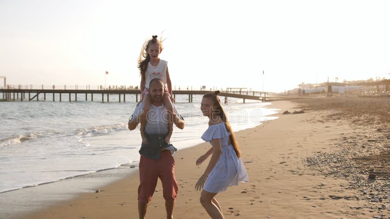 Glücklicher Vater, der sich bei SonnenunterSonnenuntergang mit ihren beiden Töchtern am Strand amüsiert Ein Mann mit einer Tochte