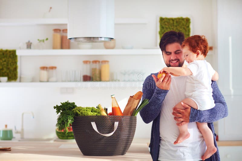 Glücklicher Vater, der Säuglingsbabysohn eine frische Frucht vom Einkaufskorb, Hauptküche anbietet stockbilder Glücklicher Vater, der Säuglingsbabysohn eine frische Frucht vom Einkaufskorb, Hauptküche anbietet stockbilder