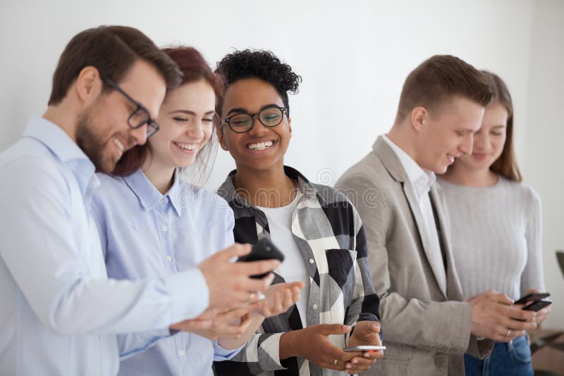Glücklicher verschiedener Stand der jungen Leute in der Reihe unter Verwendung der Smartphones lizenzfreie stockfotografie Glücklicher verschiedener Stand der jungen Leute in der Reihe unter Verwendung der Smartphones lizenzfreie stockfotografie