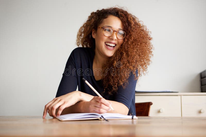 Glücklicher weiblicher Student, der am Schreibtischschreiben im Buch sitzt