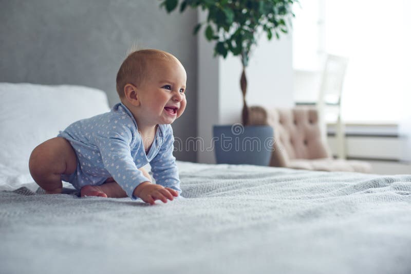 Glückliches Baby des achtmonatigen Babys, das zu Hause auf Bett kriecht lizenzfreies stockbild Glückliches Baby des achtmonatigen Babys, das zu Hause auf Bett kriecht lizenzfreies stockbild