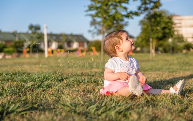 Glückliches Baby, welches das Sitzen auf einem Graspark spielt stockfotografie Glückliches Baby, welches das Sitzen auf einem Graspark spielt stockfotografie