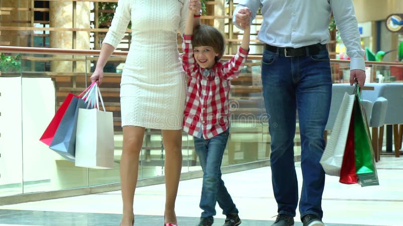 Glückliches Familien-Weihnachtseinkaufen im Mall Der Junge hält eine Hand die Mutter und der Vater Eltern und Kind mit Paketen