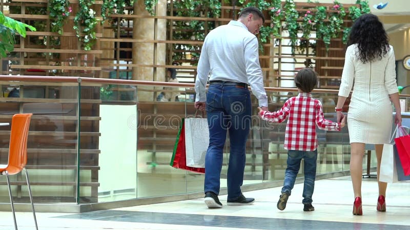 Glückliches Familien-Weihnachtseinkaufen im Mall Der Junge hält eine Hand die Mutter und der Vater Eltern und Kind mit Paketen