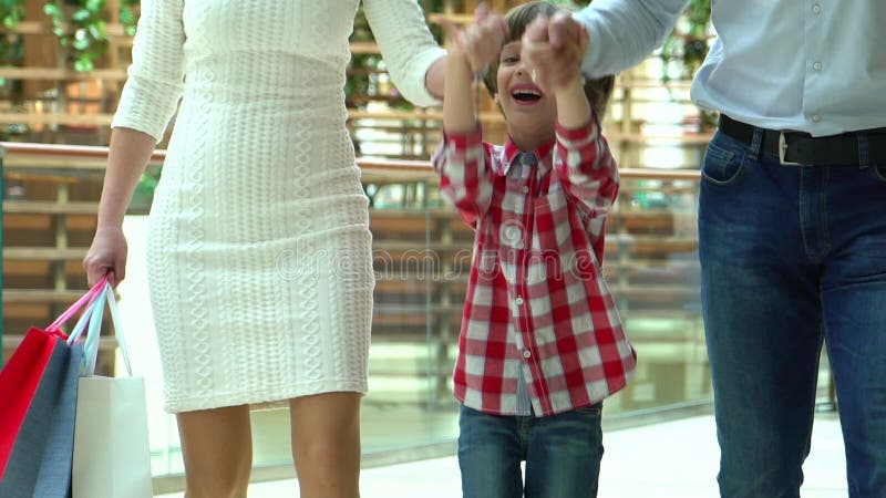 Glückliches Familien-Weihnachtseinkaufen im Mall Der Junge hält eine Hand die Mutter und der Vater Eltern und Kind mit Paketen