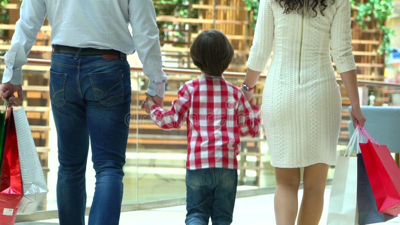 Glückliches Familien-Weihnachtseinkaufen im Mall Der Junge hält eine Hand die Mutter und der Vater Eltern und Kind mit Paketen