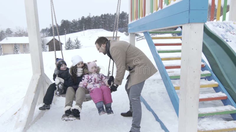 Glückliches Familienporträt auf hölzernem schwingen heraus im Winter, slowmotion