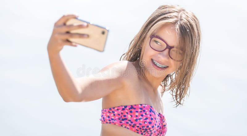 Glückliches junges Mädchen mit den zahnmedizinischen Klammern, die selfhie auf Strand am heißen Tag des Sommers machen lizenzfreie stockfotos Glückliches junges Mädchen mit den zahnmedizinischen Klammern, die selfhie auf Strand am heißen Tag des Sommers machen lizenzfreie stockfotos