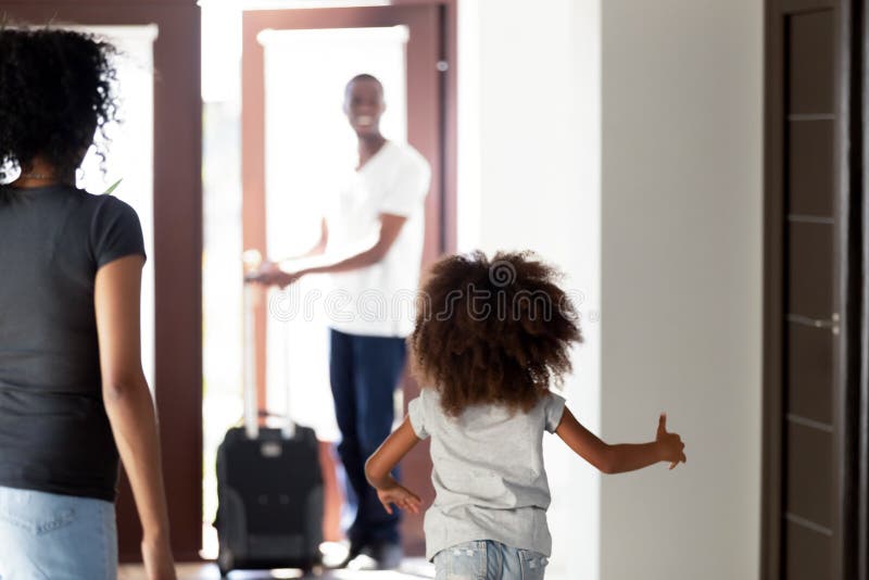 Happy child daughter running to meet african dad coming home with suitcase, rear view at little kid girl hurrying to hug father arriving after business trip, welcome back daddy, black family reunion. Happy child daughter running to meet african dad coming home with suitcase, rear view at little kid girl hurrying to hug father arriving after business trip, welcome back daddy, black family reunion