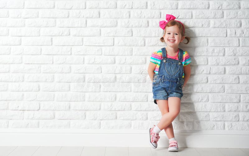 Glückliches Kinderkleines Mädchen, das über leere Backsteinmauer lacht stockfotos
