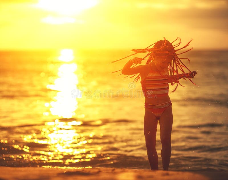 Glückliches Kindermädchen im Badeanzug mit Fliegenhaartanzen auf Strand bei Sonnenuntergang stockfotos Glückliches Kindermädchen im Badeanzug mit Fliegenhaartanzen auf Strand bei Sonnenuntergang stockfotos