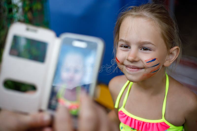 Glückliches kleines Mädchen mit dem gemalten aufwerfenden Gesicht beim auf Smartphone fotografiert werden lizenzfreies stockfoto Glückliches kleines Mädchen mit dem gemalten aufwerfenden Gesicht beim auf Smartphone fotografiert werden lizenzfreies stockfoto